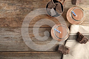 Flat lay composition with jars of tasty chocolate milk and space for text on wooden background.