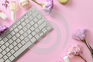 Flat lay composition with keyboard and flowers on pink background.