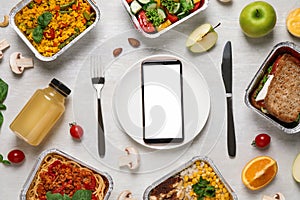 Flat lay composition with lunchboxes and smartphone on white wooden table. Healthy food delivery