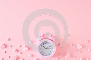Flat lay composition made of alarm clock and hearts on pastel pink background