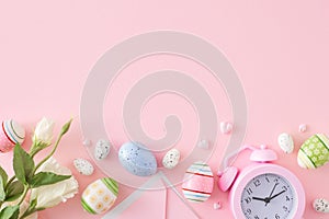 Flat lay composition made of colorful eggs, flowers, envelope and alarm clock on pastel pink background