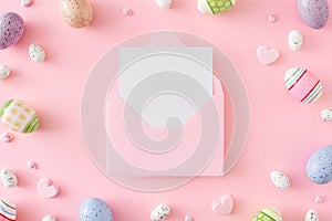 Flat lay composition made of colorful eggs, pink hearts on pastel pink background and envelope