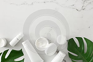 Flat lay composition made of cosmetic bottles, cream jars, green tropical leaves on marble background