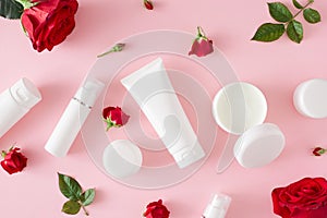 Flat lay composition made of cosmetic bottles without label, cream jars and red flowers with leaves