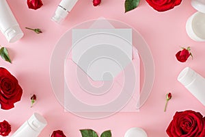 Flat lay composition made of cosmetic bottles, red roses with leaves on pastel pink background