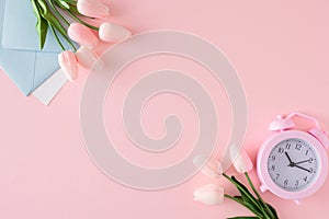 Flat lay composition made of envelope, spring flowers and alarm clock on pastel pink background