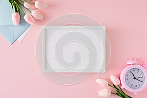 Flat lay composition made of envelope, spring flowers, alarm clock and white frame in the middle