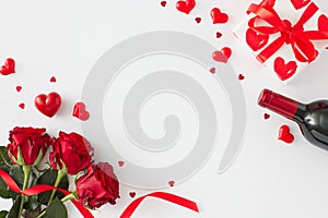 Flat lay composition made of red roses with ribbon, wine bottle, gift box, red hearts on white background
