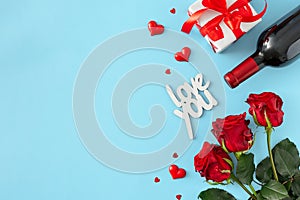 Flat lay composition made of red roses, wine bottle, gift box, red hearts, inscription love you