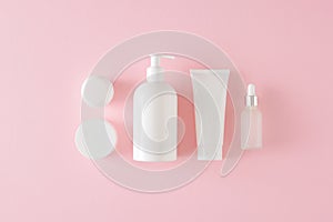 Flat lay composition made of white cosmetic bottles, cream jars and dropper bottle on pastel pink background