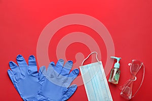 Flat lay composition with medical gloves, mask and hand sanitizer on red background. Space for text