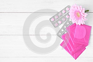 Flat lay composition with menstrual pads, pills and flower on white wooden table. Gynecology concept photo