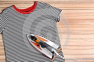 Flat lay composition with modern electric iron and t-shirt on wooden table