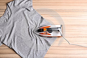 Flat lay composition with modern electric iron and t-shirt on wooden table