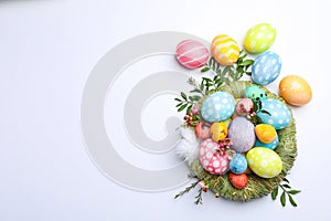 Flat lay composition with nest, Easter eggs, feathers and flowers on color background