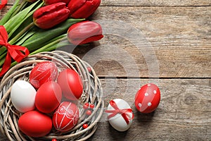 Flat lay composition of nest with painted Easter eggs and flowers on wooden table