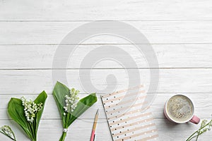 Flat lay composition with notebook, lily of the valley bouquets and coffee on white wooden background.