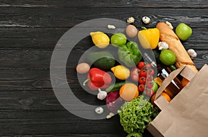 Flat lay composition with overturned paper bag and groceries on black wooden . Space for