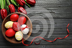 Flat lay composition of painted Easter eggs and flowers on wooden table, space for text