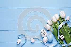 Flat lay composition of painted Easter eggs and tulip flowers on light blue wooden table. Space for text