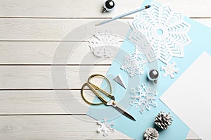 Flat lay composition with paper snowflakes, scissors and Christmas decoration on white wooden background, space for text