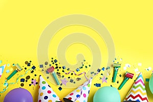 Flat lay composition with party hats, balloons and confetti on yellow background, space for text. Birthday decor