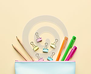 Flat lay composition of pastel blue pencil case with pens, pencils,paper binders.Copy space,beige background.Top view on various