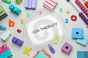 Flat lay composition with phrase ABA Therapy and colorful toys on white wooden table photo