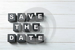 Flat lay composition with phrase SAVE THE DATE made of black cubes on wooden background