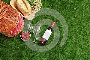 Flat lay composition with picnic basket, wine and strawberries on grass