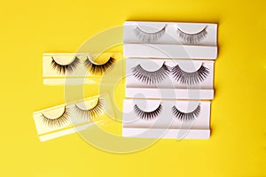 Flat lay composition of professional makeup tools and false eyelashes on bright yellow background, space for text. Concept of make