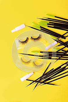 Flat lay composition of professional makeup tools and false eyelashes on bright yellow background, space for text. Concept of make