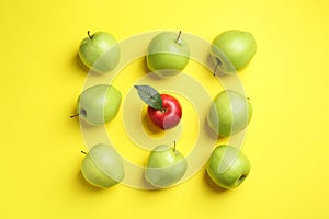 Flat lay composition with red apple surrounded by green ones on yellow background