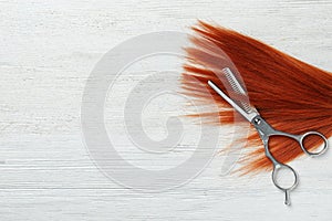 Flat lay composition with red hair, thinning scissors and space for text on white wooden background.