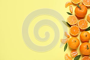 Flat lay composition with ripe tangerines and leaves on light yellow background, space for text. Citrus fruit