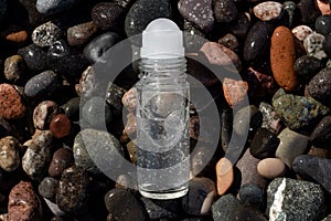 Flat lay composition of a roll on transparent deodorant bottle on wet beach stones