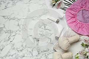 Flat lay composition with shower cap and toiletries on white marble background. Space for text
