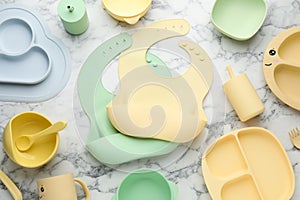 Flat lay composition with silicone baby bibs and plastic dishware on white marble background