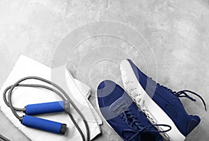 Flat lay composition with sneakers, jumping rope and towel on grey background. Gym workout