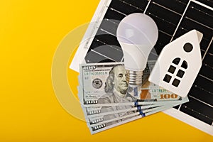 Flat lay composition with solar panel, led lamp, house model and money on table.