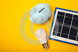 Flat lay composition with solar panel, led lamp and piggy bank on background.