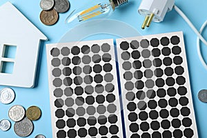 Flat lay composition with solar panels, house model, light bulb and and coins on blue background
