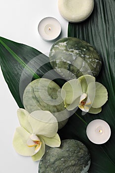 Flat lay composition with spa stones, green leaves and beautiful flowers on white table