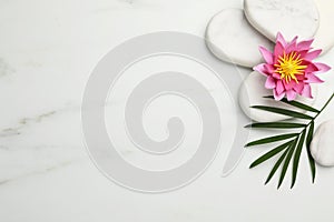 Flat lay composition with spa stones, lotus flower and leaf on white marble table. Space for text