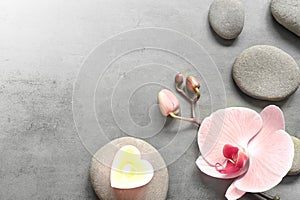 Flat lay composition with spa stones, orchid pink flower and heart on grey.