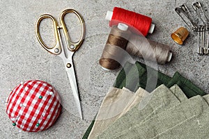 Flat lay composition with spools of threads and sewing tools on light textured table