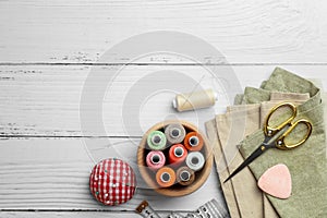 Flat lay composition with spools of threads and sewing tools on white wooden table, space for text