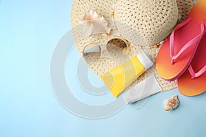 Flat lay composition with sunscreen and beach accessories on light blue background, space for text