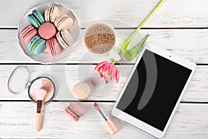 Flat lay composition with tasty macarons, tablet computer and cosmetic products on wooden background