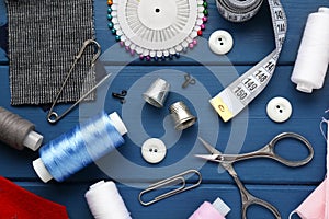 Flat lay composition with thimbles and different sewing tools on blue wooden table